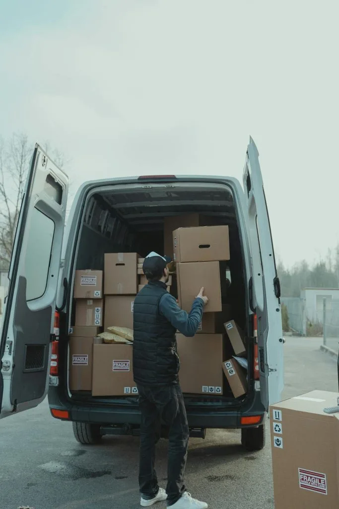 A delivery worker loading cardboard boxes into a van, preparing for shipment outdoors.