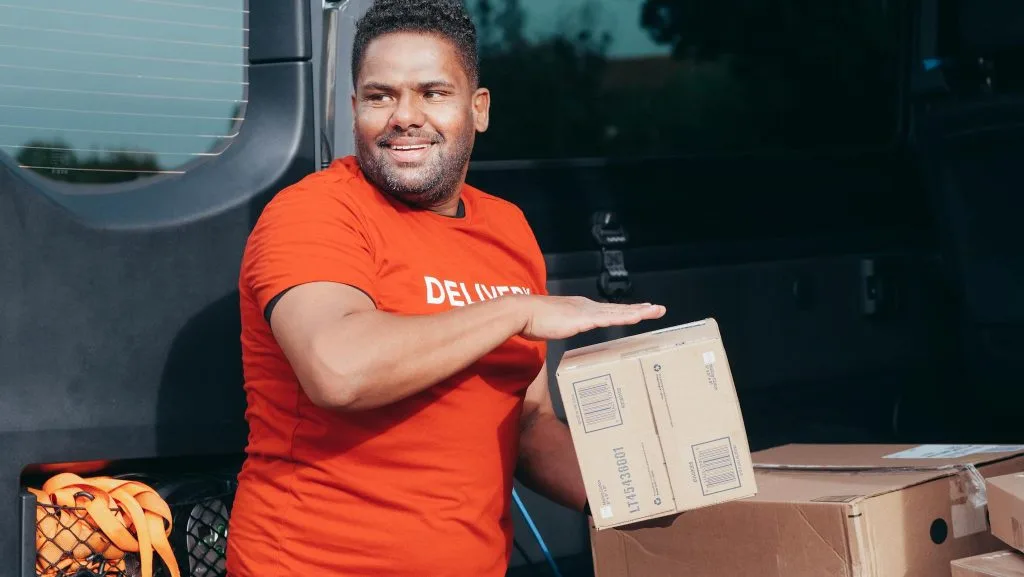 Smiling delivery man handling packages from van during daytime courier service.