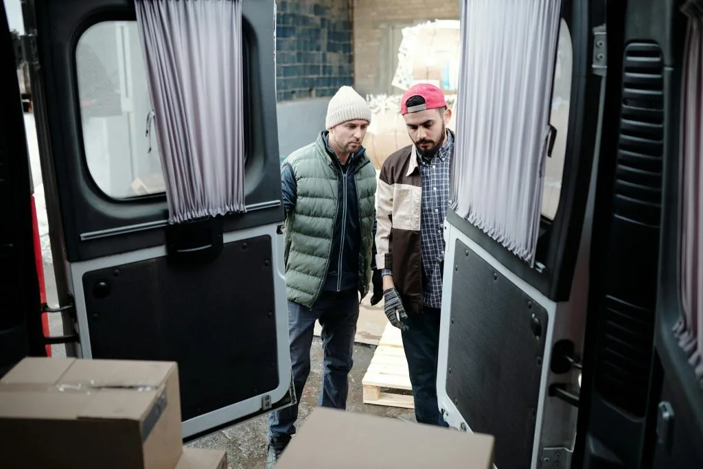 Two delivery workers load parcels into a van, focusing on efficiency and teamwork.